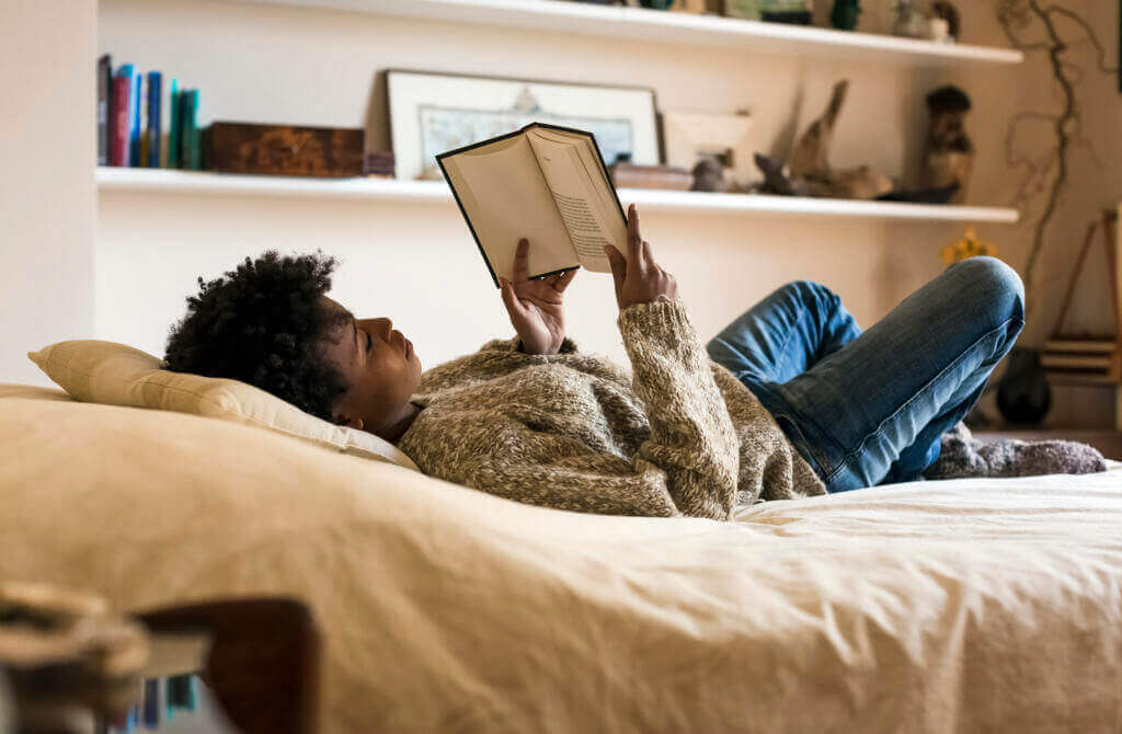 Young Woman Lying on Bed Reading a Book - Good E-reader